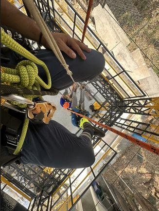 Manos con guante manipulando cuerda y bloqueador en estructura